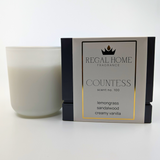 A white candle next to its packaging box, which is labeled 'Countess' scent no. 100 and includes notes of lemongrass, sandalwood, and vanilla.