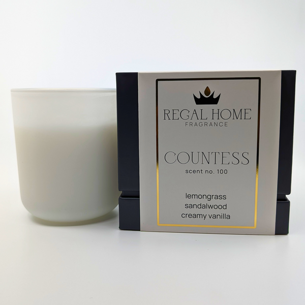 A white candle next to its packaging box, which is labeled 'Countess' scent no. 100 and includes notes of lemongrass, sandalwood, and vanilla.
